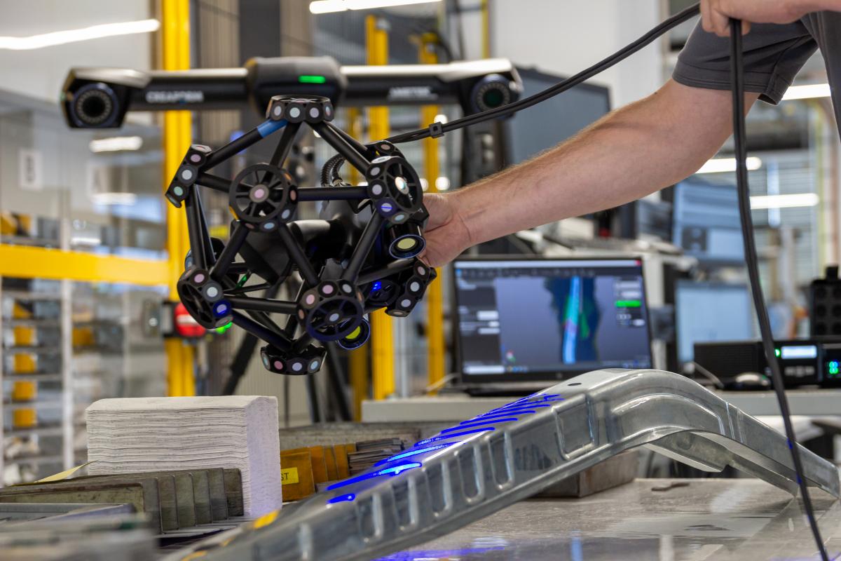 MetraSCAN 3D 扫描仪扫描一个钣金部件。在背景中,您可以看到笔记本电脑上的实时扫描数据。